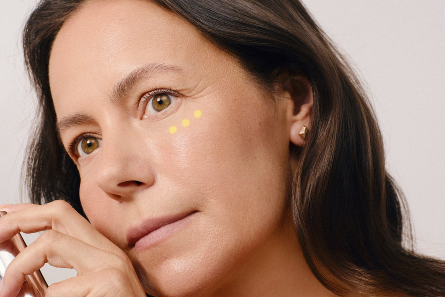 Close-up of a woman in her 50s resting her fingers on her jaw, with dots of eye cream under one eye