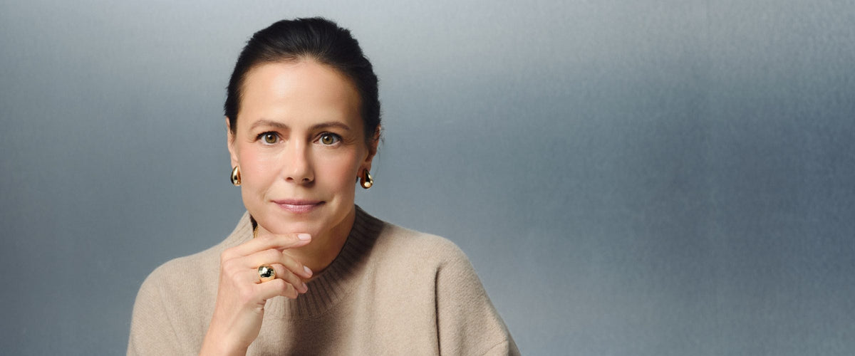 Woman in her late 40s in a beige sweater sitting at a white table with a MISOORA serum