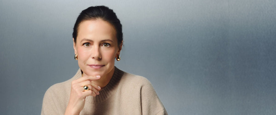 Woman in her late 40s in a beige sweater sitting at a white table with a MISOORA serum